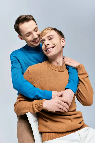 Two stylish men, a loving gay couple, sit closely together on a gray backdrop. — Stock Photo
