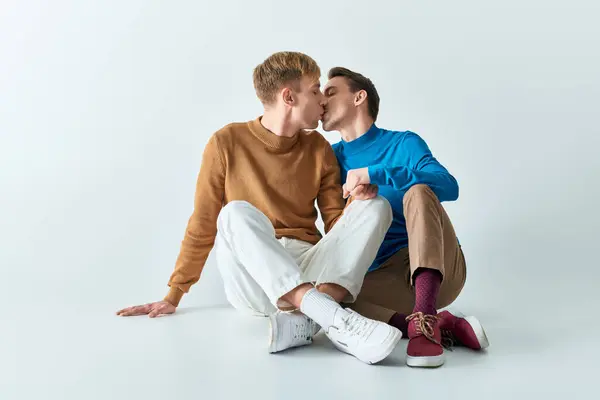 Two young men in casual clothes sitting on the ground kissing each other. — Stock Photo
