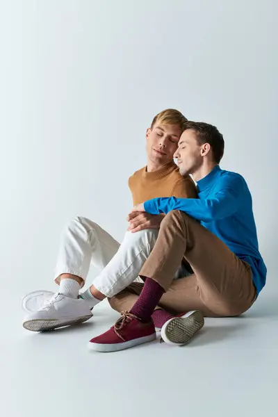 Two men in casual attire sitting on the ground, arms wrapped around each other in a loving embrace. — Stock Photo