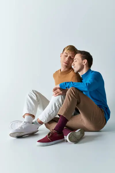 Dos hombres en atuendo casual sentados en el suelo, los brazos envueltos uno alrededor del otro en un abrazo amoroso. — Stock Photo