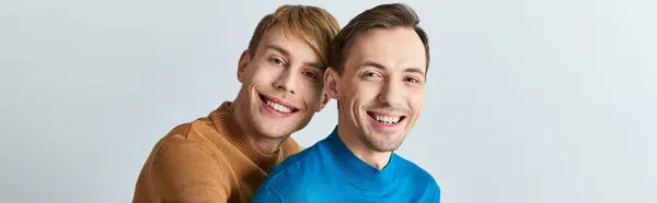 Two men in casual attire embrace each other on a gray backdrop, symbolizing love and unity. — Stock Photo