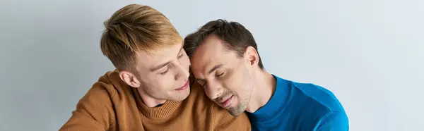 Two loving gay men in casual attire sitting closely on a gray backdrop. — Stock Photo