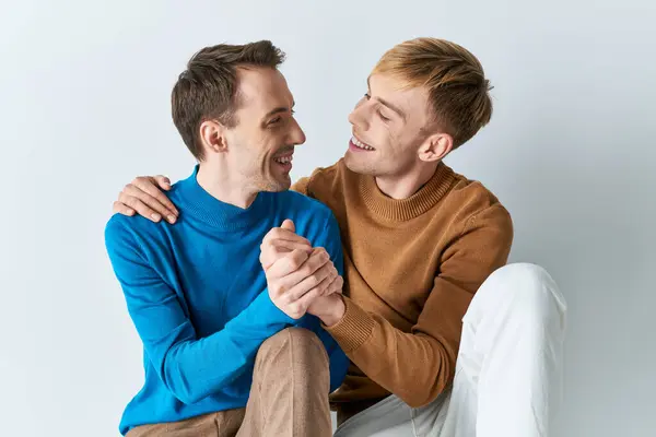 Two men in casual attire sharing a joyful moment on a gray backdrop. — Stock Photo