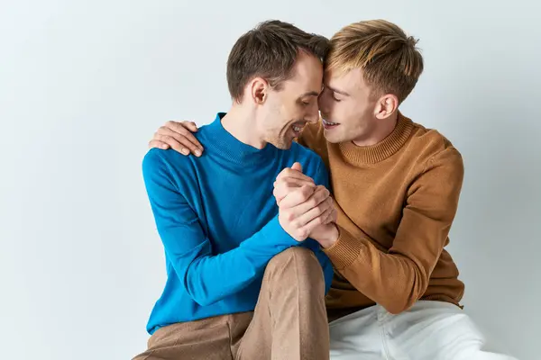 Two men in casual attire sitting on a white surface, showcasing a loving bond. — Stock Photo