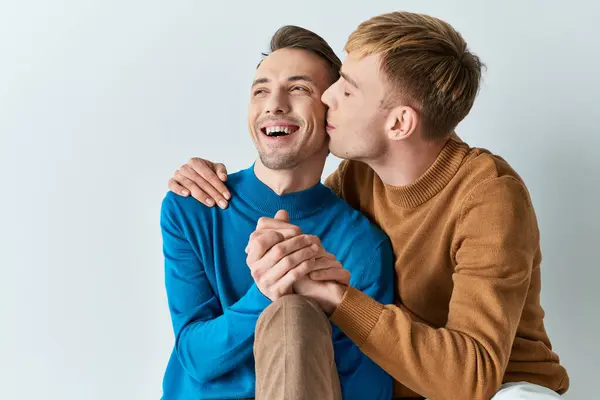 A gay couple in casual attire sitting closely together on a gray backdrop. — Stock Photo