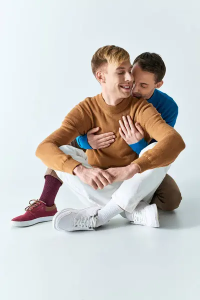 Two men in casual attire sitting on the ground, hugging each other closely. — Stock Photo