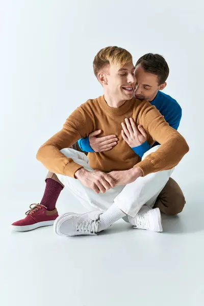 Due uomini in abbigliamento casual seduti a terra, che si abbracciano strettamente. — Foto stock