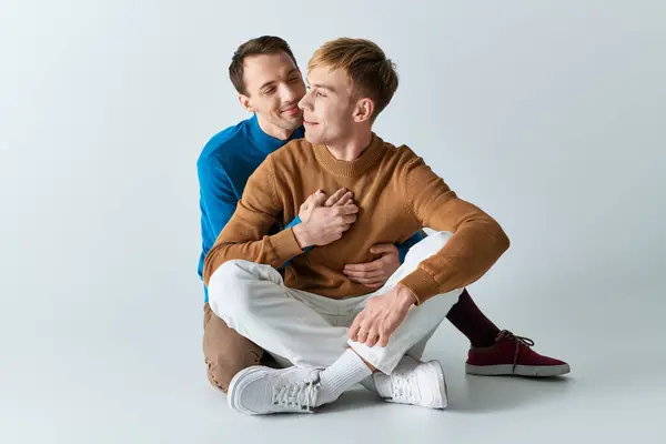 Two men in casual attire sit on the ground with arms around each other. — Stock Photo