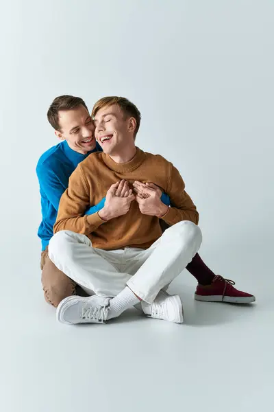 Dos hombres con atuendo casual, sentados en el suelo, compartiendo un abrazo. - foto de stock