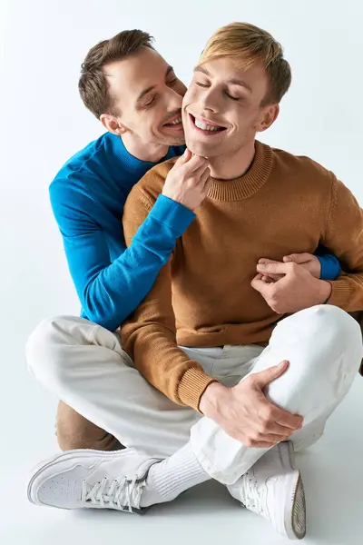 Two men sit on the ground, smiling happily as a loving gay couple in casual attires. — Stock Photo