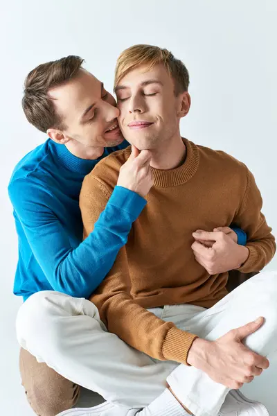 Un amour gay couple dans casual attires partage un tendre baiser tandis que assis sur un tabouret. — Photo de stock