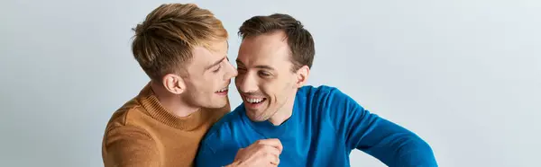 Dos hombres, una pareja gay amorosa, con atuendo casual, parados uno al lado del otro en un fondo gris. - foto de stock