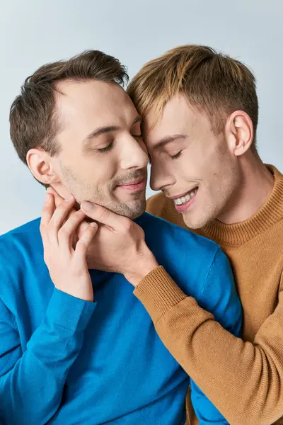 Two people hugging affectionately, a loving gay couple in casual attire, against a gray backdrop. — Photo de stock