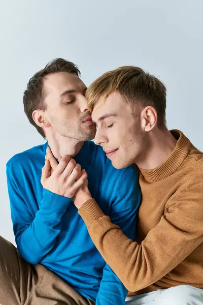 Una pareja gay amorosa con atuendo casual sentada una al lado de la otra en un fondo gris. — Stock Photo