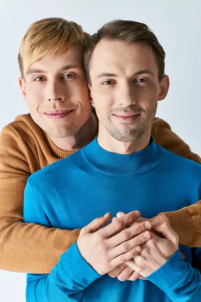 A loving gay couple in casual attire embrace each other against a gray backdrop. — Stock Photo