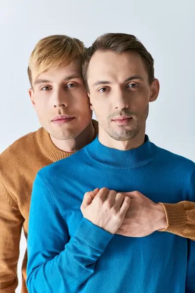 Una pareja gay amorosa con atuendo casual posan juntos sobre un fondo gris. - foto de stock