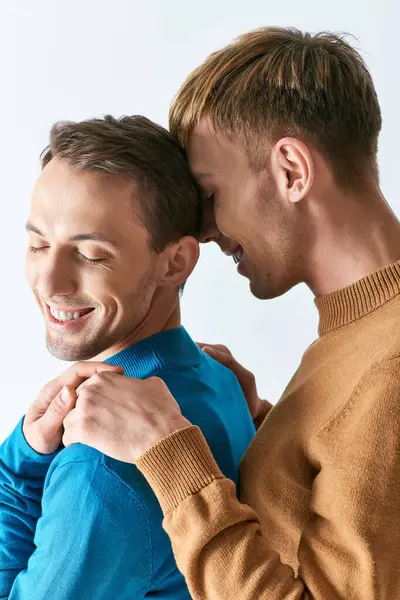 A loving gay couple in casual attire standing together on a gray backdrop. — Stock Photo