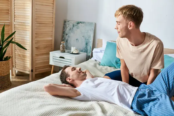 Two men in casual attire lying on a bed, sharing a tender moment together. — Stock Photo
