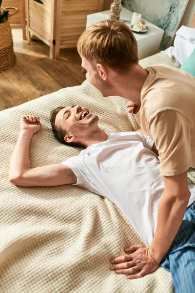 Un hombre acostado encima de una cama junto a otro hombre. - foto de stock