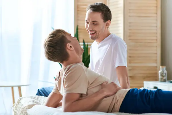 Un hombre recibiendo un masaje de espalda de su pareja en un ambiente acogedor. - foto de stock