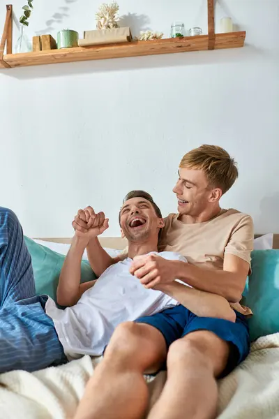 Two men in casual attire sit closely together on a bed. — Stock Photo