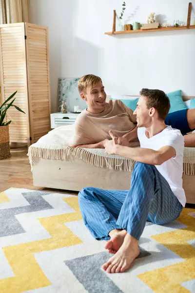Dois homens, um casal gay amoroso, sentam-se graciosamente em cima de um sofá de traje casual, curtindo a companhia uns dos outros.. — Fotografia de Stock
