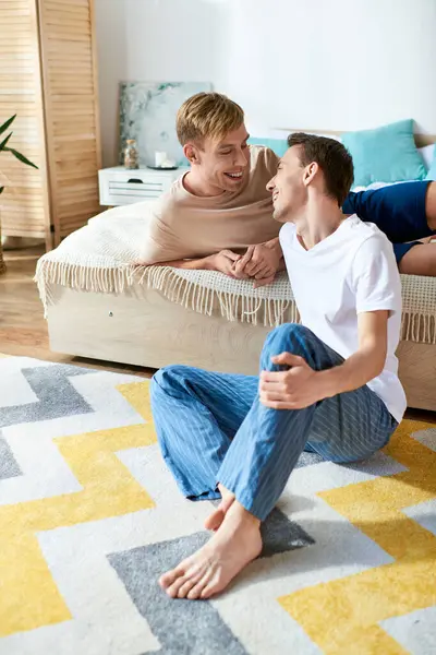 Two men in casual attire sitting close together on a bed. — Stock Photo