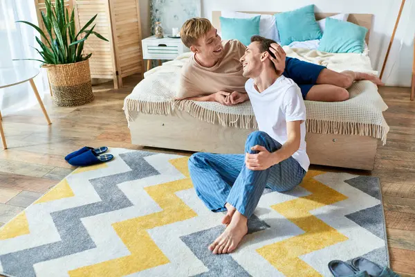 Dos hombres se sientan juntos en una cama, compartiendo un momento de tranquilidad y unión. - foto de stock