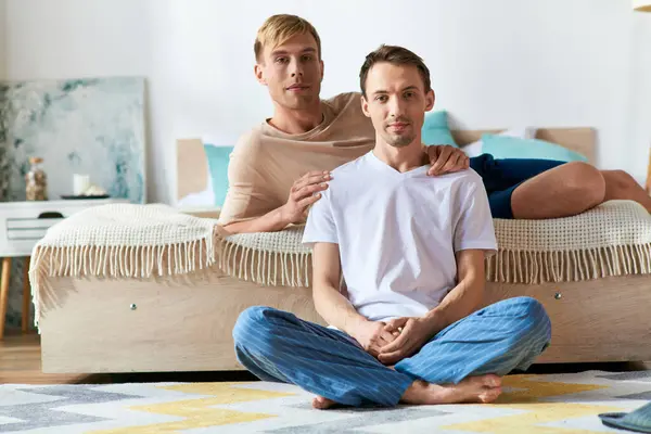 Two casually dressed men share an intimate moment sitting atop a bed. — Stock Photo