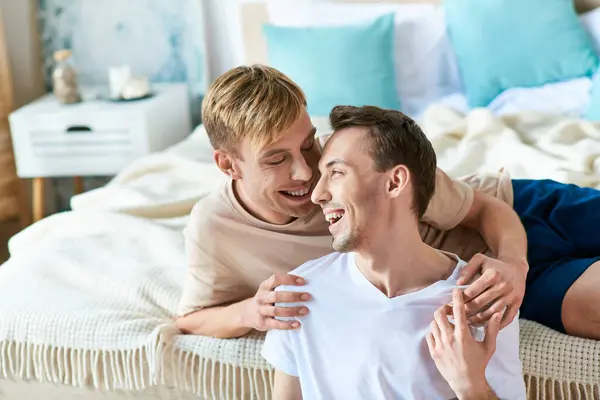 Two men in casual attire lie intertwined on a bed, exuding comfort and connection. — Photo de stock