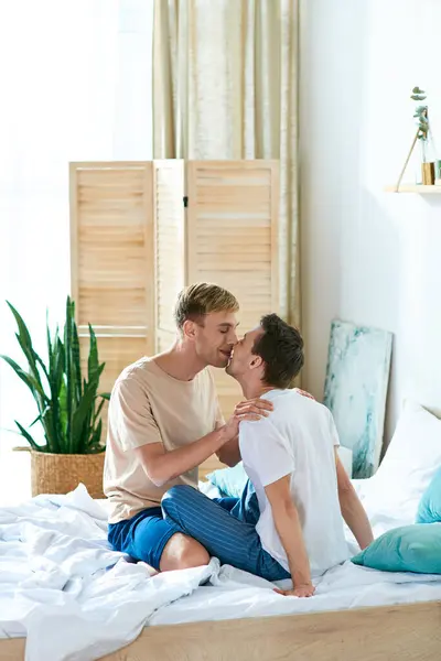 A loving gay couple in casual attire sharing a kiss while sitting on a bed. — Stock Photo