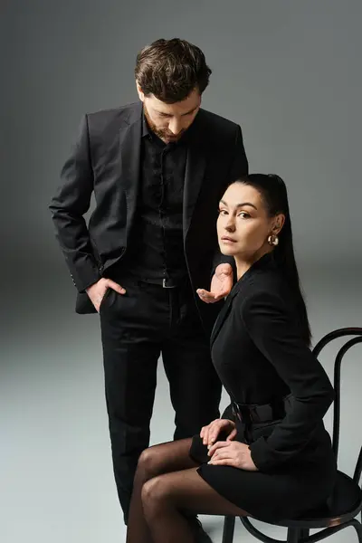 A man stands next to a woman in a black dress, both looking elegant and captivating. — Stock Photo