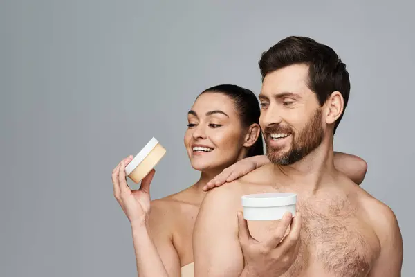 Jolly couple elegantly hold a jar of cream, showcasing their skincare routine. — Stock Photo