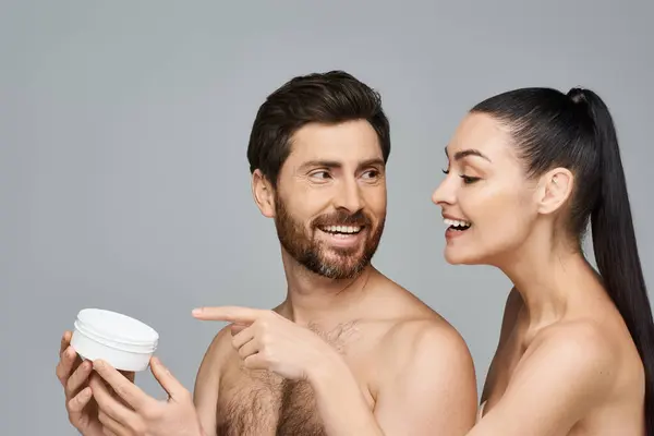 Allegro coppia elegantemente tenere un vaso di crema, in mostra la loro routine di cura della pelle. — Foto stock