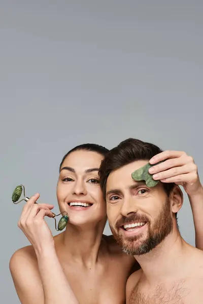 Fröhliches Paar, strahlende Schönheit, mit Gesichtsroller und Gua-sha zusammen. — Stockfoto