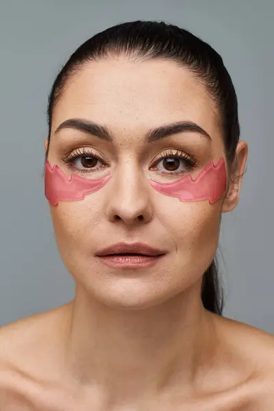 Donna con toppe rosa applicate sul viso, in posa per un trattamento di cura della pelle. — Foto stock