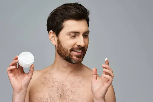 A shirtless man holds a jar of cream. — Stock Photo