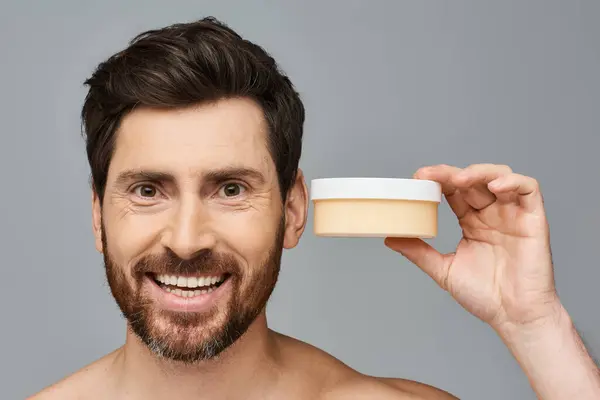A man smiling, holding a jar of cream, applying it to his face. — Stock Photo