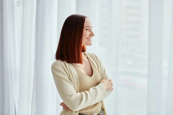 A young woman stands in contemplation in front of a window. — Stock Photo
