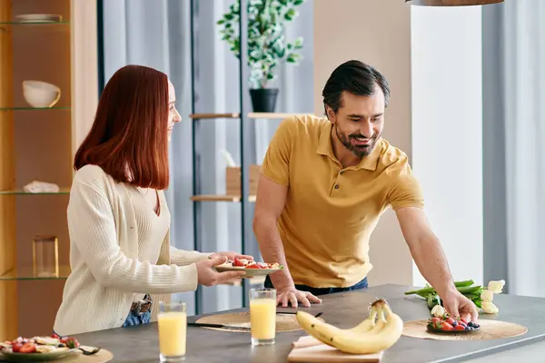 Uma mulher ruiva e um homem barbudo preparam comida juntos em uma cozinha moderna, mostrando trabalho em equipe e unidade. — Fotografia de Stock