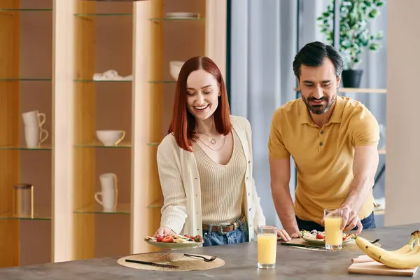 A redhead woman and bearded man prepare ingredients and cook together in a modern apartment kitchen. — Stock Photo