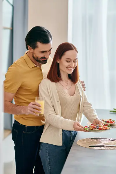 Рыжая женщина и бородатый мужчина смеются и едят еду на современной кухне, создавая счастливые воспоминания вместе. — стоковое фото