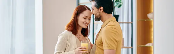 Um belo casal adulto, uma mulher ruiva e um homem barbudo, desfrutando de um copo de suco de laranja juntos em um apartamento moderno. — Fotografia de Stock