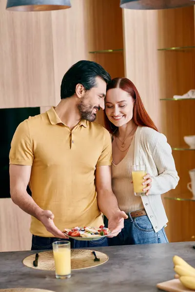 Una donna rossa e un uomo barbuto si trovano in una cucina moderna, con un piatto di frutti colorati. — Foto stock