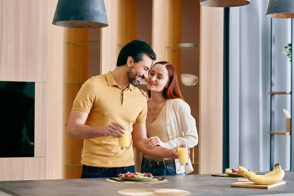Рыжая женщина и бородатый мужчина разделяют уютный момент, стоя вместе на современной кухне. — стоковое фото