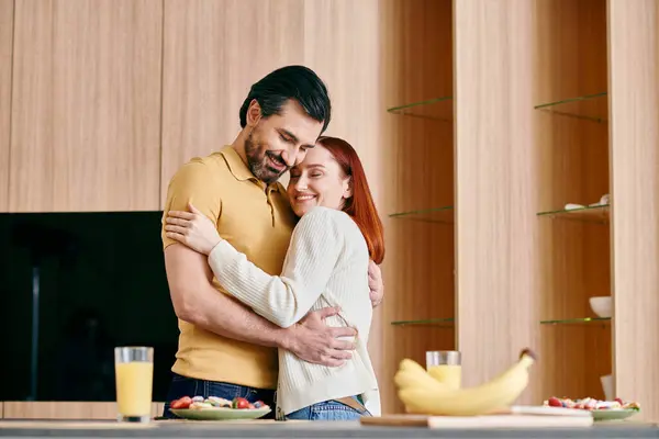 A redhead woman and bearded man share a warm embrace in a modern kitchen, laughing and cherishing the moment together. — Stock Photo