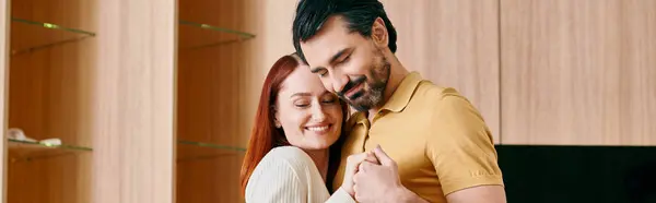 Un beau couple d'adultes, une femme rousse et un homme barbu partagent un câlin sincère dans leur salon moderne. — Photo de stock