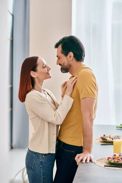 A bearded man and a redhead woman embrace in a warm kitchen, enjoying a moment of togetherness in their modern apartment. — Stock Photo