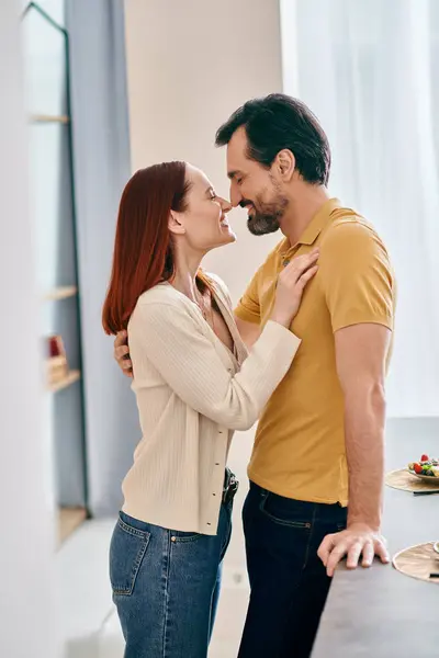 Una rossa e un uomo barbuto che condividono un bacio appassionato in una cucina moderna, esprimendo amore e connessione. — Foto stock