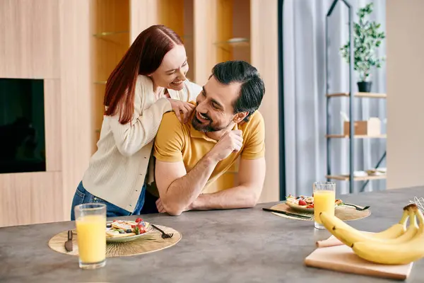 Uma mulher ruiva bonita e um homem barbudo desfrutando de um café da manhã tranquilo juntos em sua cozinha moderna. — Fotografia de Stock